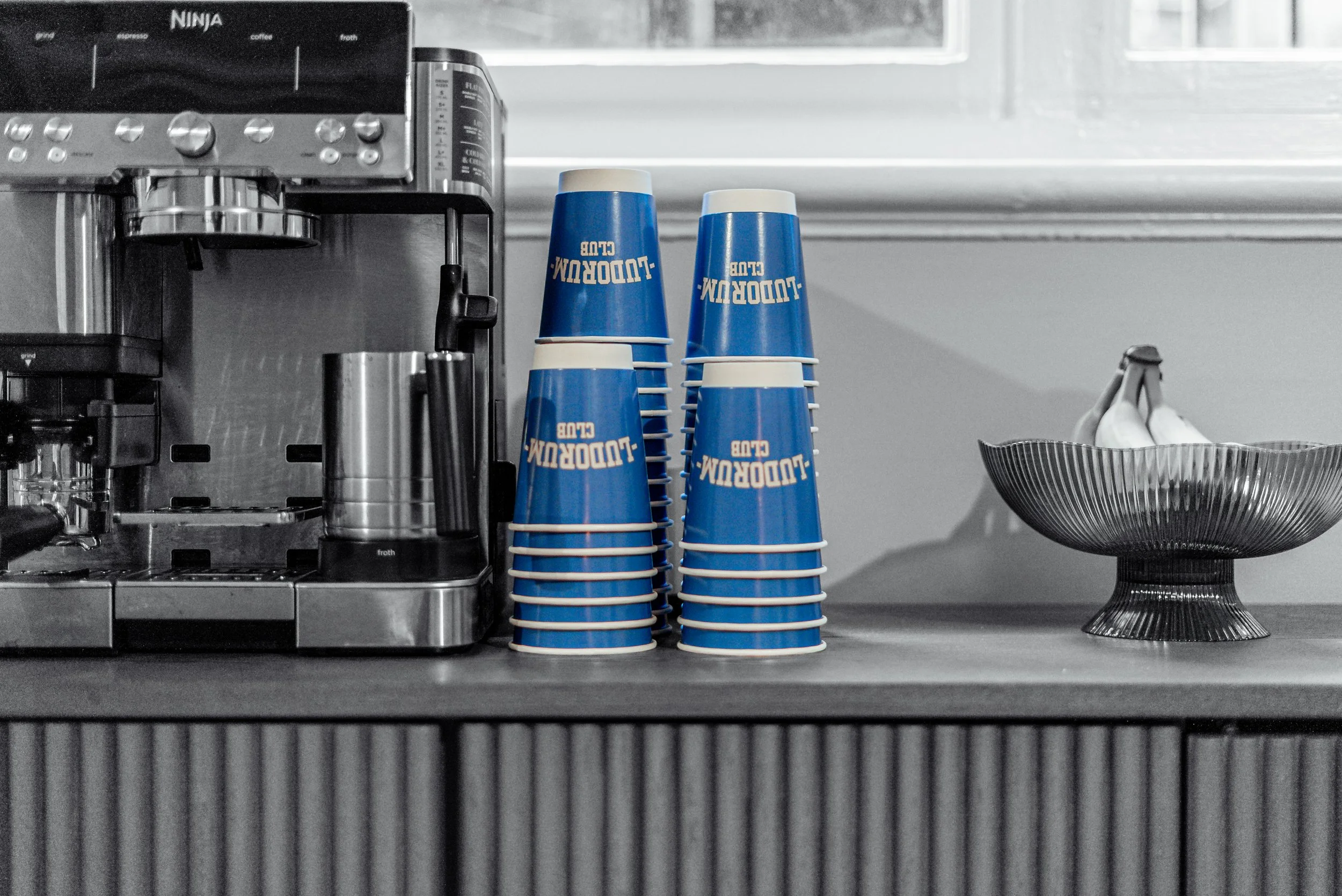 Stacks of blue Ludorum Club paper cups beside the coffee machine