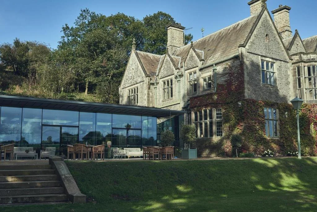 Wildhive Callow Hall, a Victorian stone country house above a lawn, with a glass extension and a terrace